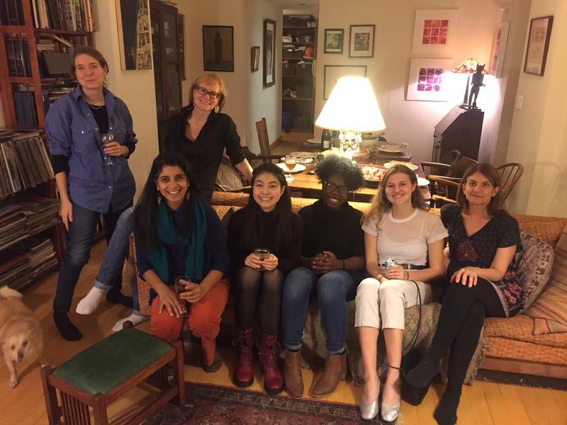 5 young women seated on a couch, 2 older women standing nearby